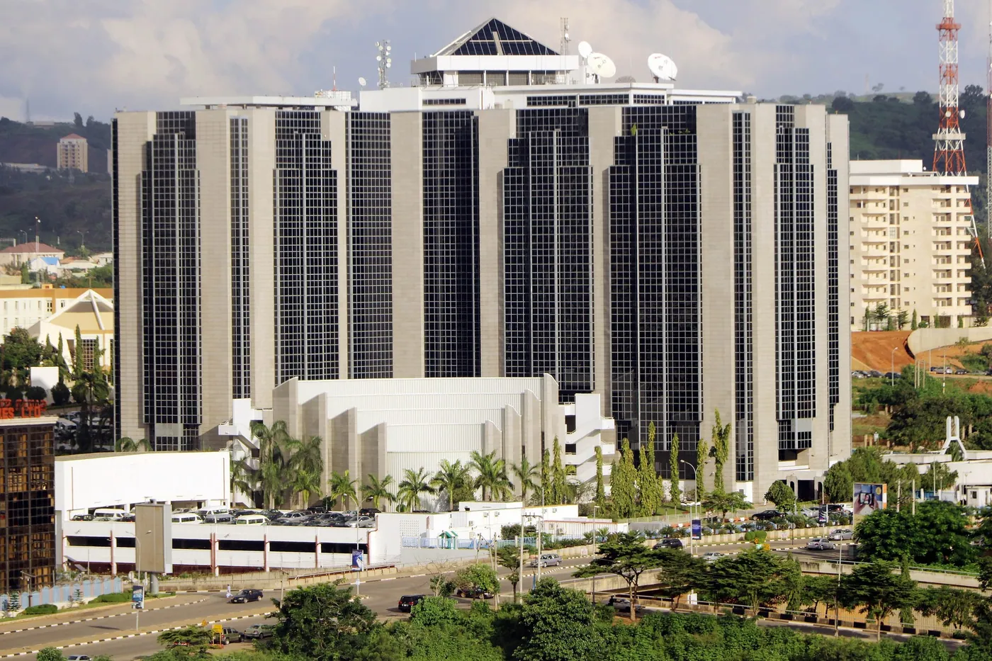 The Central Bank of Nigeria headquarters in Abuja, a dark glass and stone tower block behind palm trees and a car park