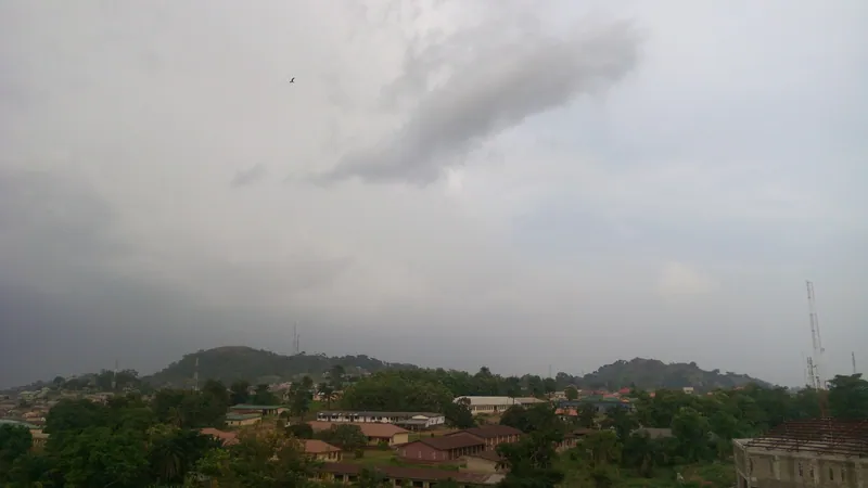 Ado-Ekiti seen from a rooftop under heavy cloud, with low hills behind the town