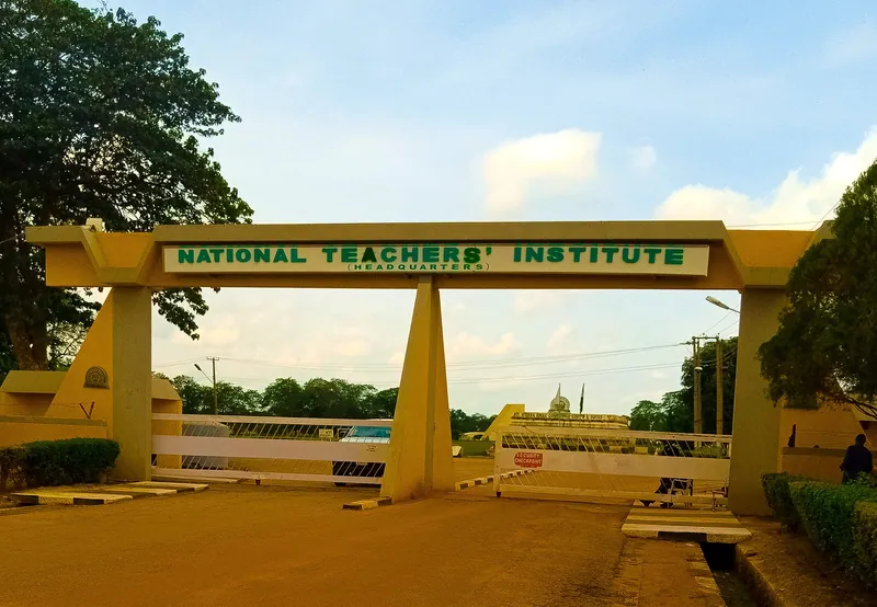 The entrance gate of the National Teachers' Institute headquarters in Kaduna, with its name in green letters across a…