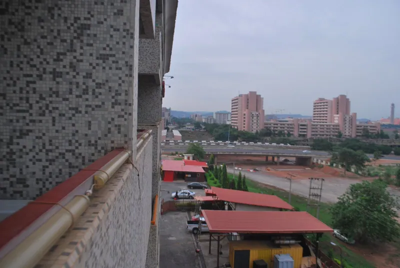 A view from a tiled balcony across Abuja's central area, with pink high-rise office blocks, a flyover and red-roofed…