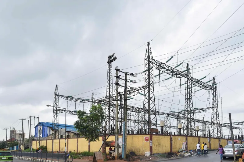 Steel lattice gantries and high voltage lines of an electricity transmission point behind a yellow wall beside a road…