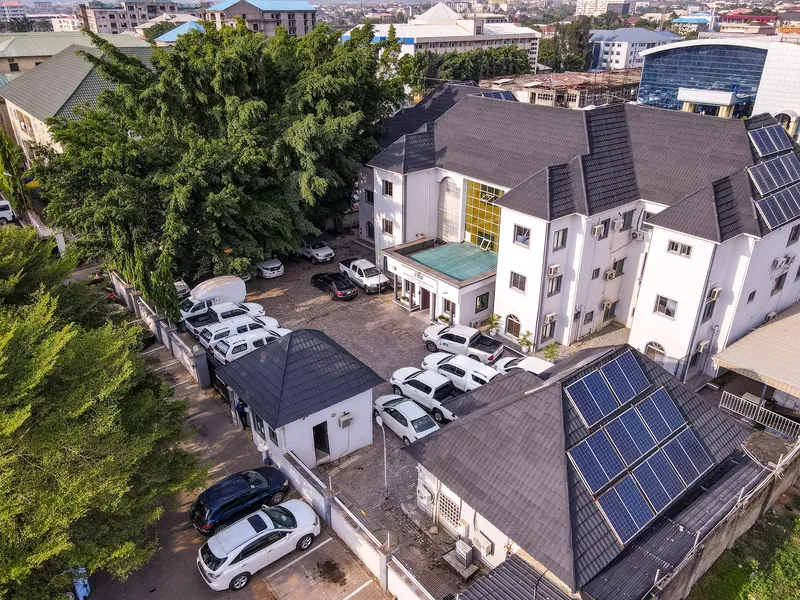 Aerial view of a white three-storey office building with grey roofs and solar panels, cars parked in its compound…