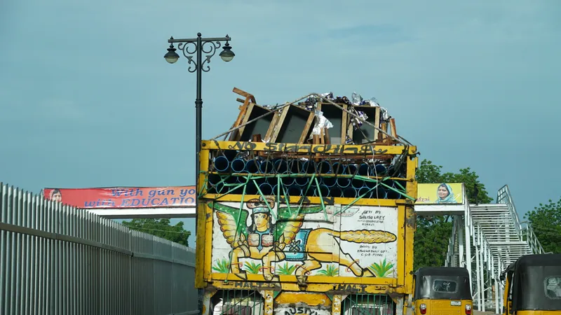 A painted goods lorry and yellow tricycles pass under a pedestrian bridge on a road in Maiduguri, Borno State