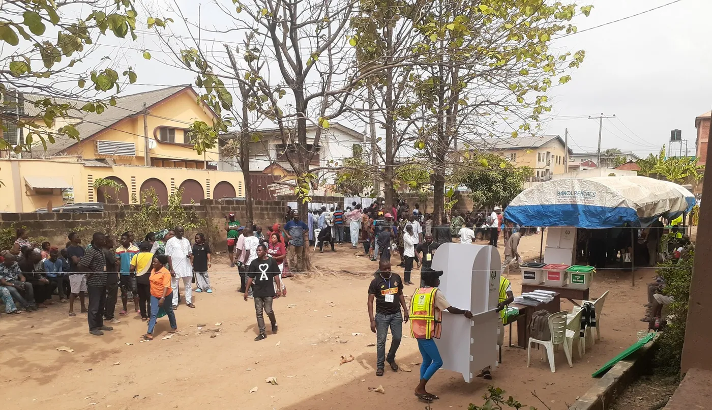 Voters and polling officials at a polling unit during Nigeria's 2023 general elections, with ballot boxes and a voting cubicle